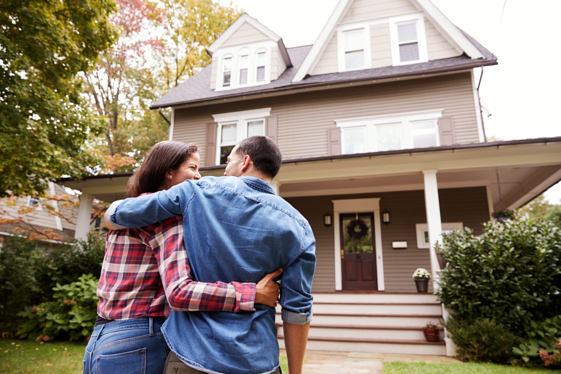 A view of a happy couple in front of a light brown craftsman-style home, to illustrate how we protect Your Property, Your Tenants, and Your Long-Term Investment Goals