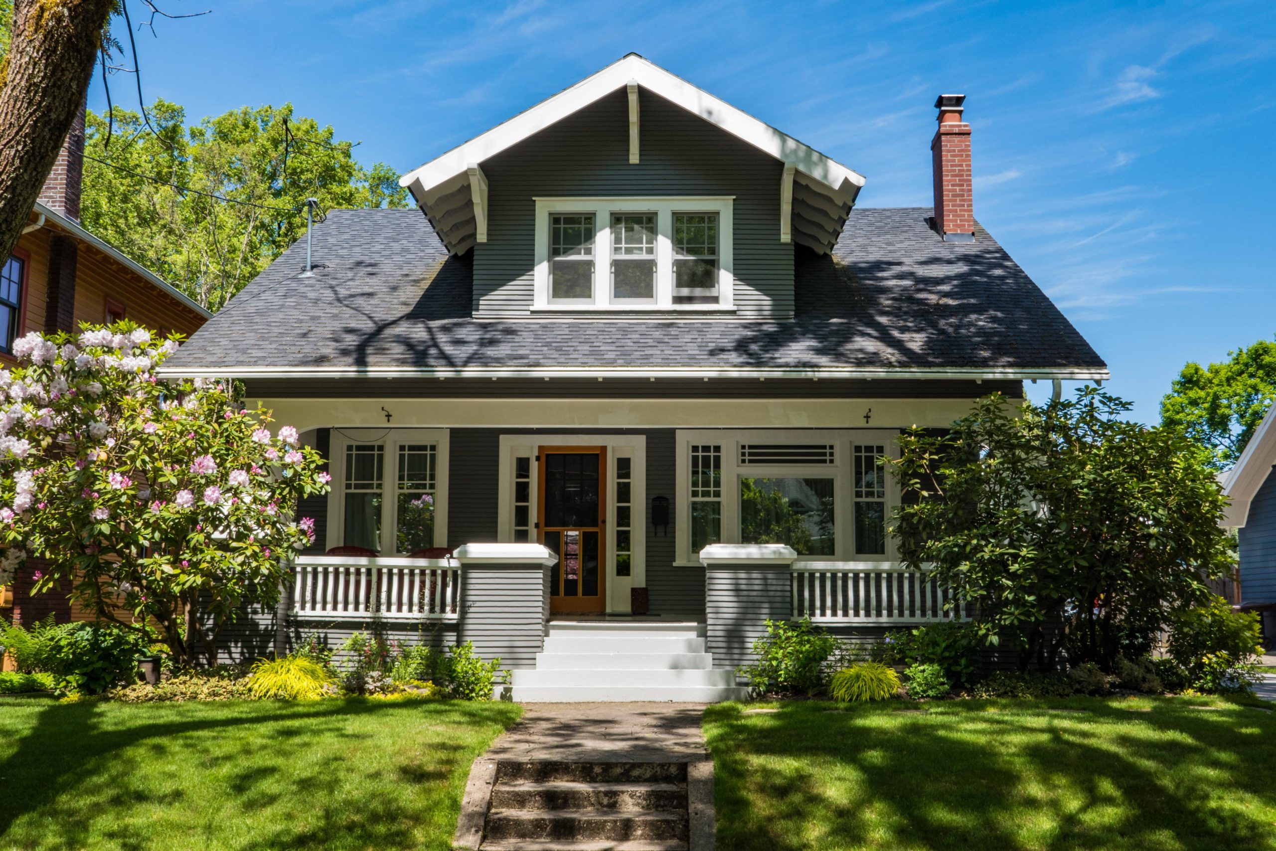 The front of a grey, craftsman style home with a green lawn