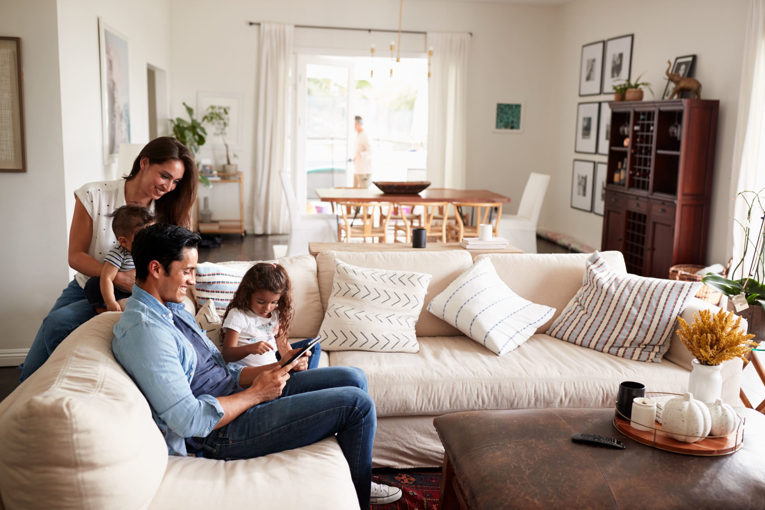 A Happy Family sitting around a white sectional in a cozy white dining room looking at an iPad, possibly searching for Homes for Rent in Santa Rosa, California